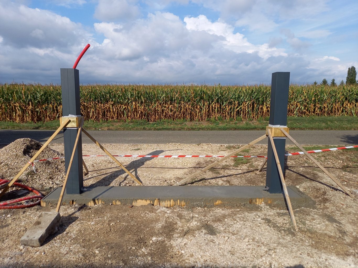 Scellement des poteaux Poteaux en métal soutenus par des cordes, avec un champ de maïs en arrière-plan.