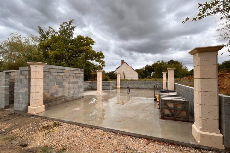 Chantier avec piliers en pierre et sol en béton sous un ciel nuageux.