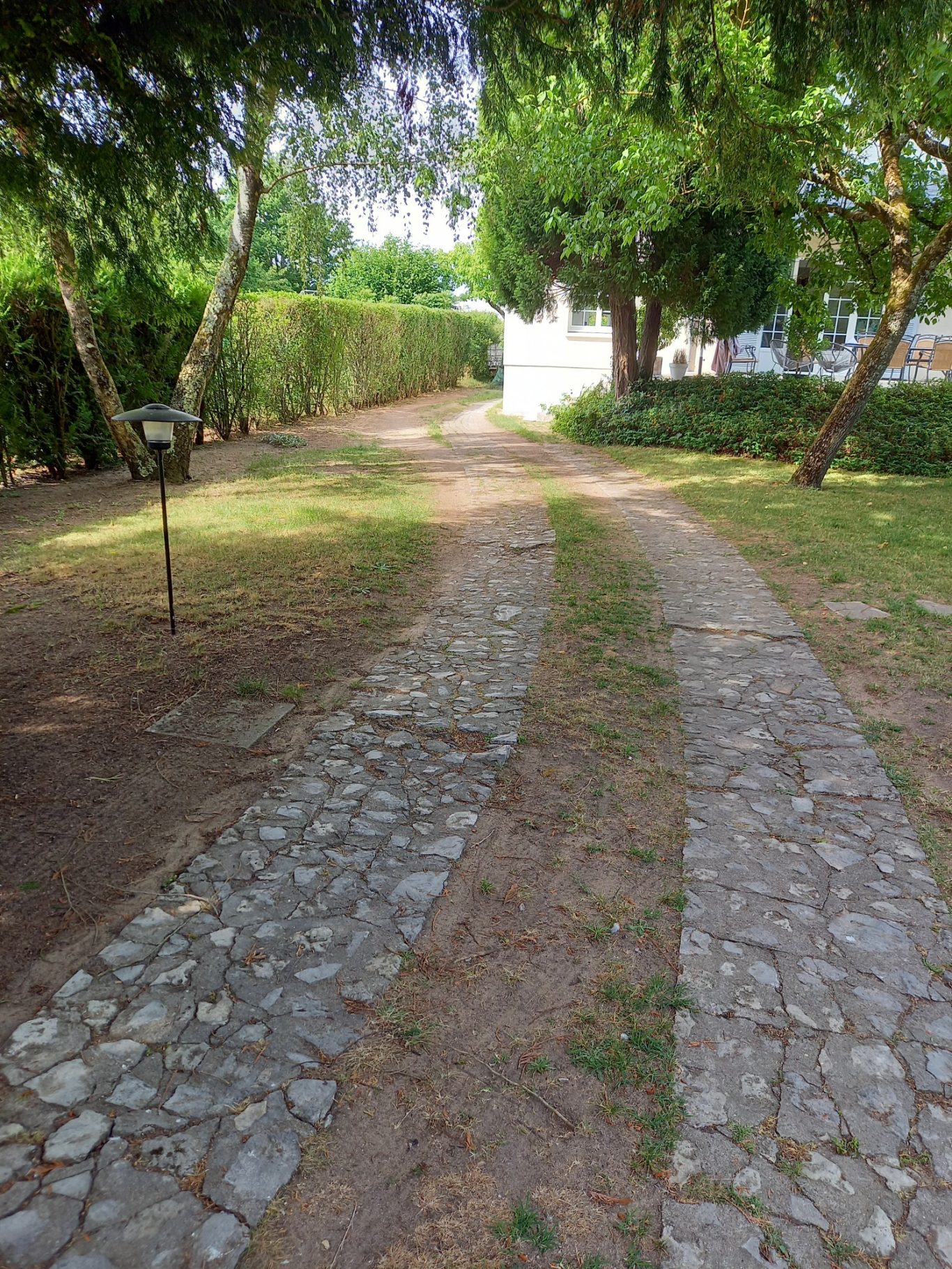 Ancienne allée Allée en pierre avec herbe et buissons de chaque côté, menant à une maison blanche.