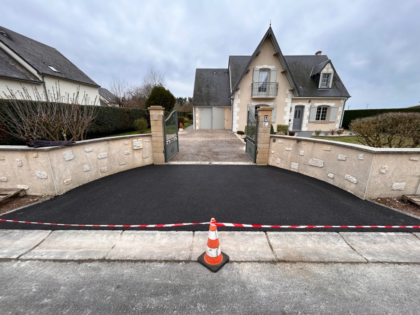 Accès en enrobé à froid Entrée avec un chemin d’accès refait, maison en arrière-plan, cône de signalisation devant.