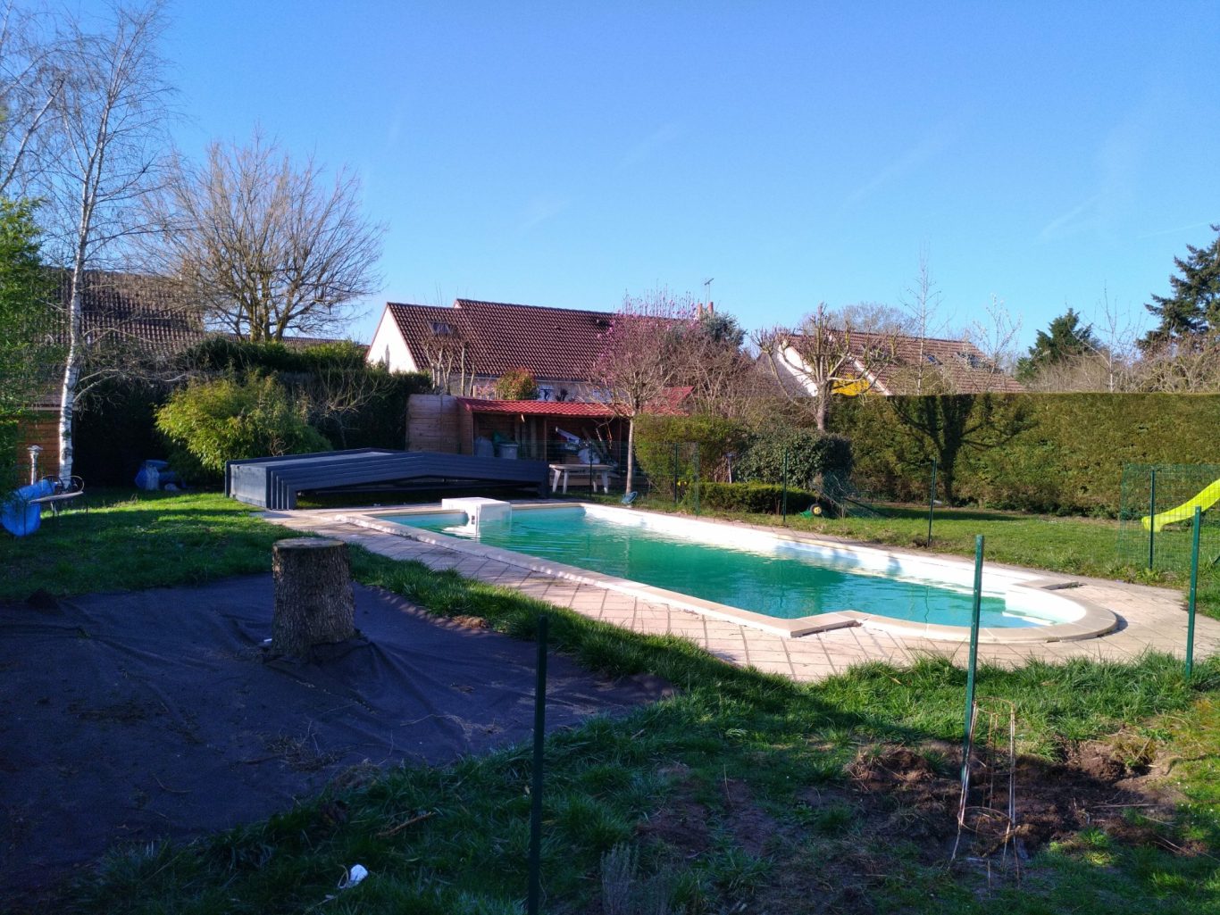 Début de chantier Piscine entourée de verdure et maison, ciel bleu dégagé.