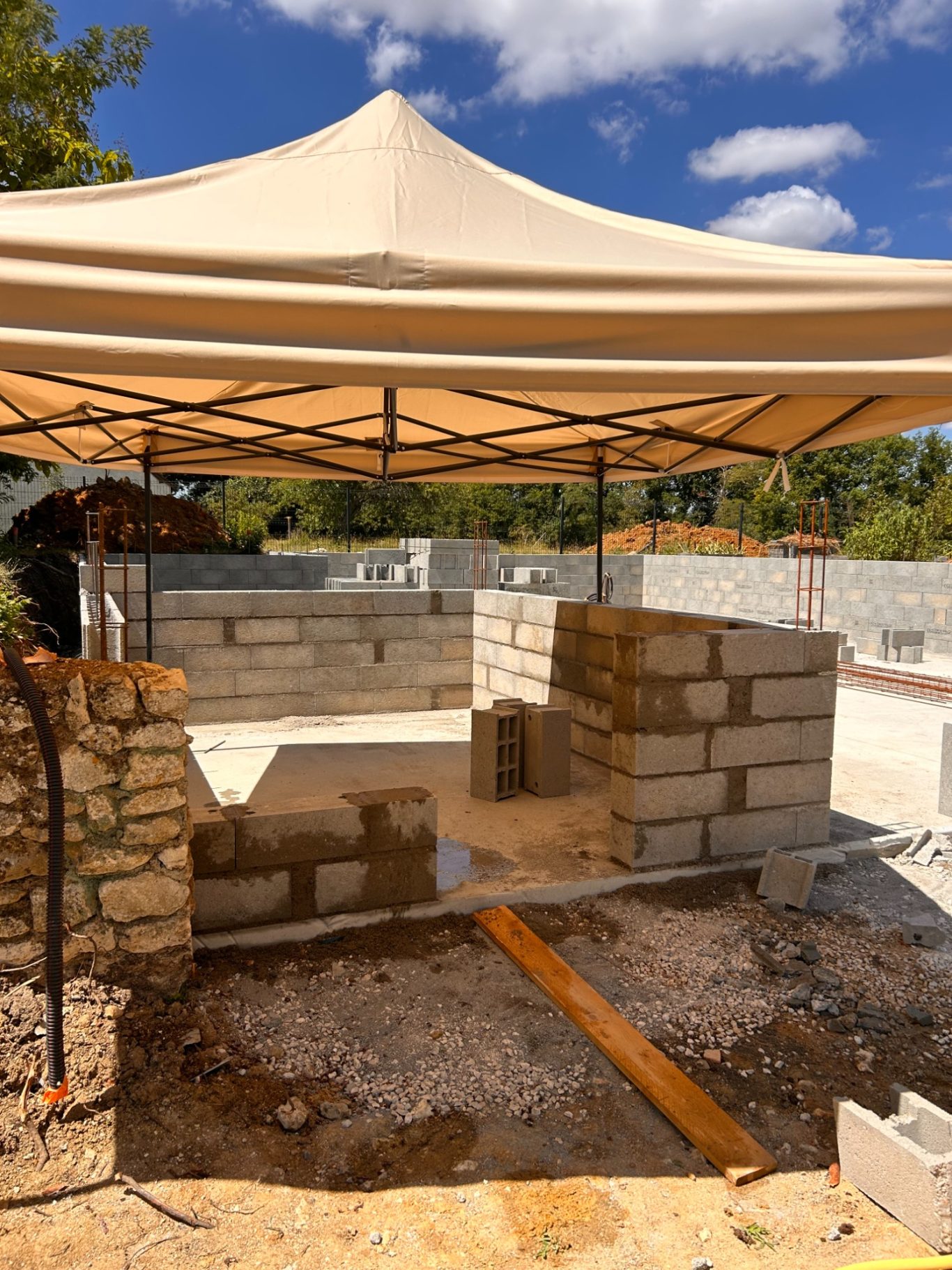 Construction d'une cave extérieure Construction site with a tent sheltering unfinished stone structure and wooden planks.