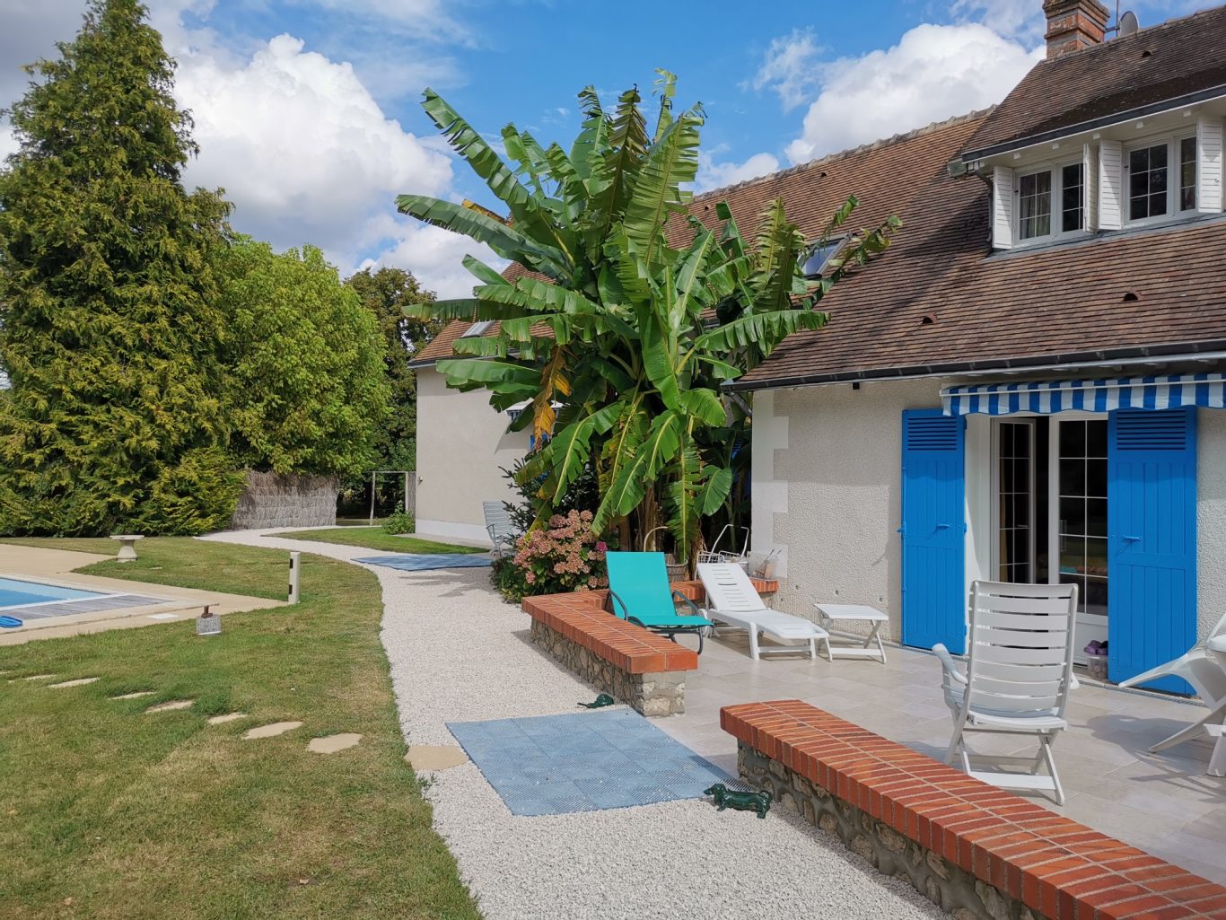 Allée en marbre blanc Terrasse avec chaises longues et palmier, bordant une piscine, sous un ciel nuageux.
