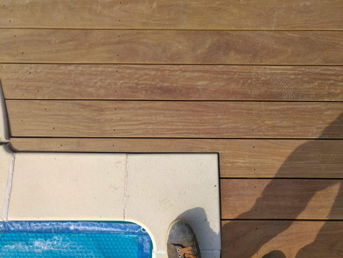 Découpe de finition Vue d'un sol en bois, avec une partie carrelée et un angle de piscine.