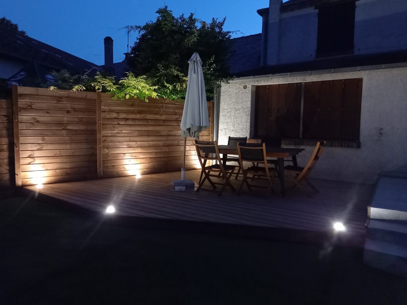 Spot encastré sur terrasse Terrasse éclairée la nuit avec table, chaises et parasol.
