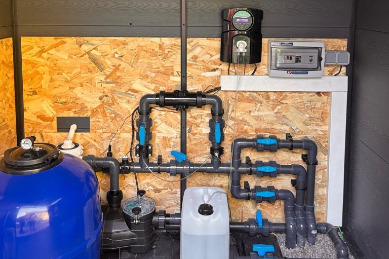 Système de plomberie intérieure avec tuyaux noirs et accessoires bleus sur mur en bois.