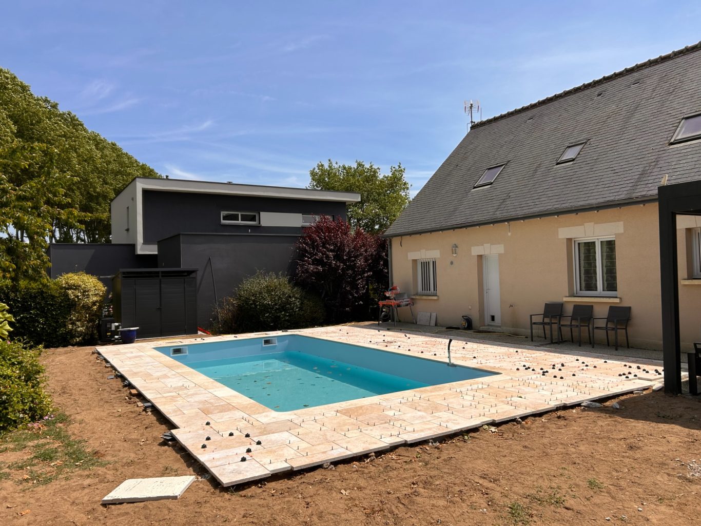 Terrasse en travertin / Pose du liner / Remplissage Maison avec piscine, terrasse en carrelage et jardin verdoyant.