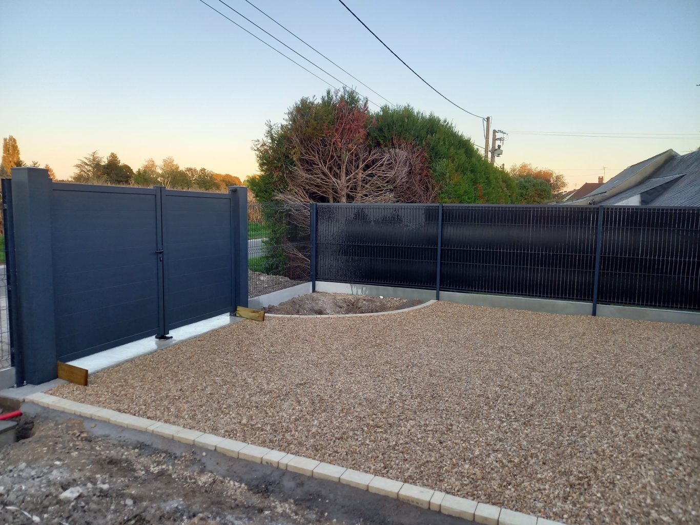 Portail / Clôture en panneaux rigides Espace extérieur avec des graviers et une clôture noire en arrière-plan.