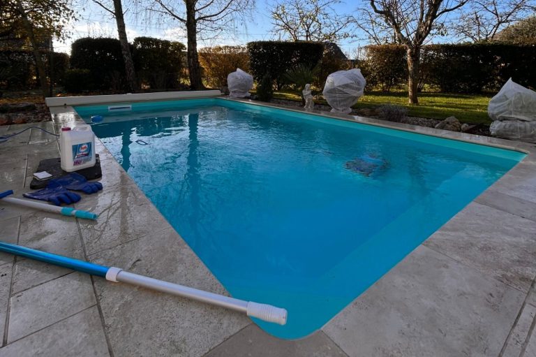 Piscine avec eau claire, entourée de pelouse et d'arbres, matériel de nettoyage à proximité.