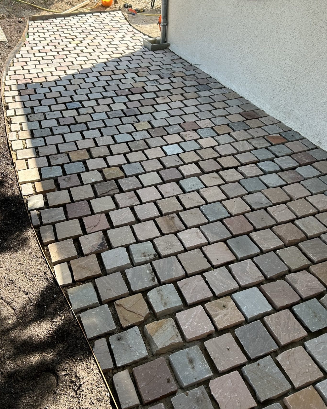 Pavage en grès Kandla Allée en pavés en béton de différentes teintes, éclairée par le soleil.