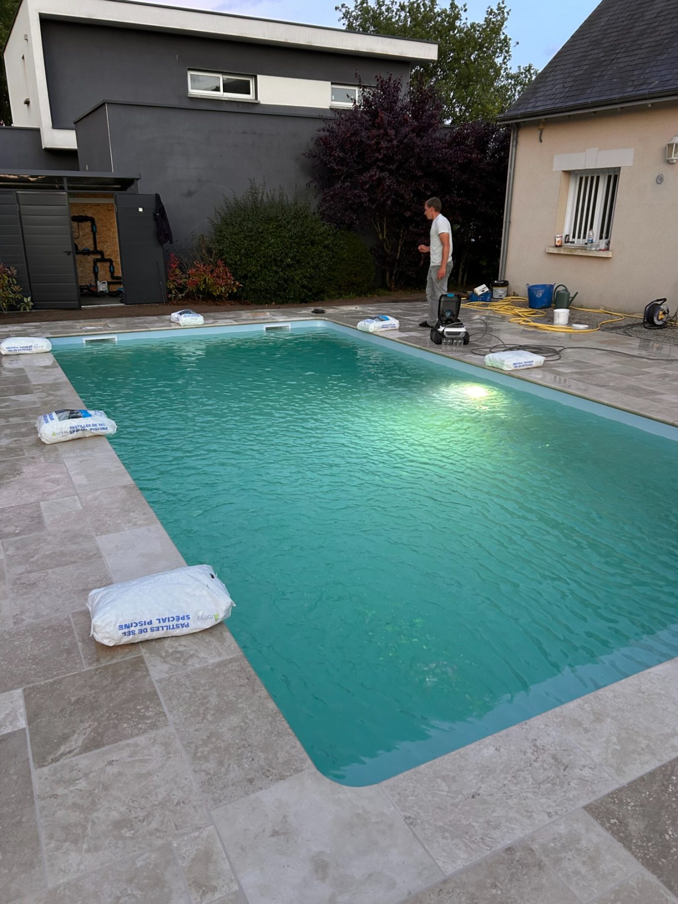 Mise en service d'un électrolyseur Piscine turquoise dans un jardin, avec une personne à proximité et des équipements autour.