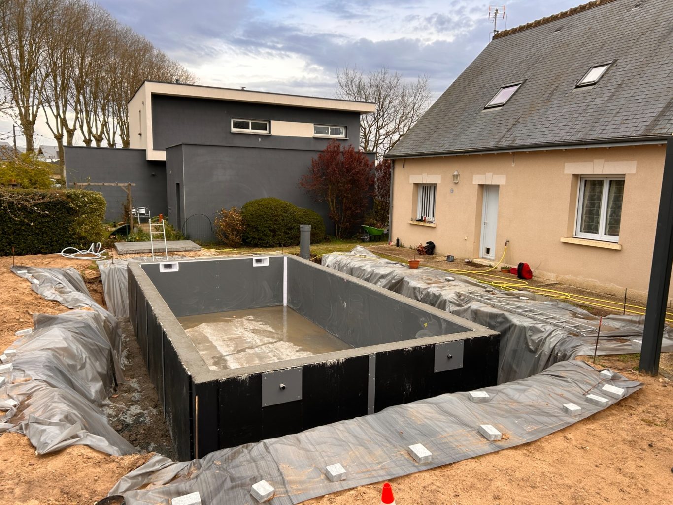 Coulage des murs Construction d'une piscine en cours, entourée de gravier et de bâches, près d'une maison.