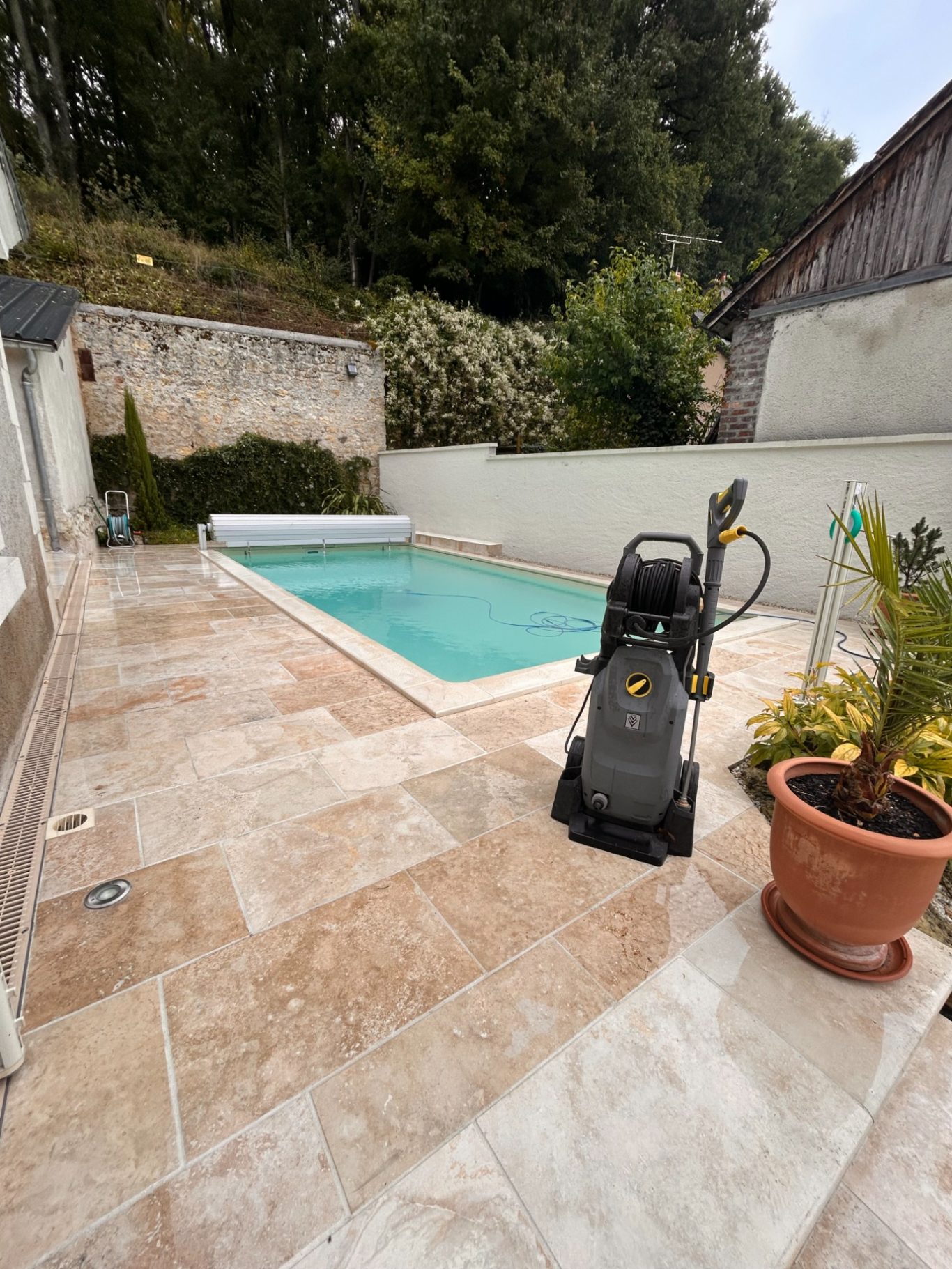 Nettoyage des abords de la piscine Piscine avec terrasse en pierre et nettoyeur de piscine à proximité.