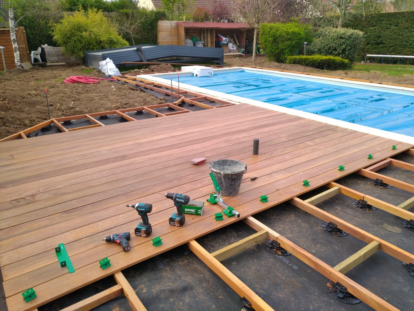 Pose des lames Terrasse en bois en cours d'installation près d'une piscine, avec outils et matériaux visibles.
