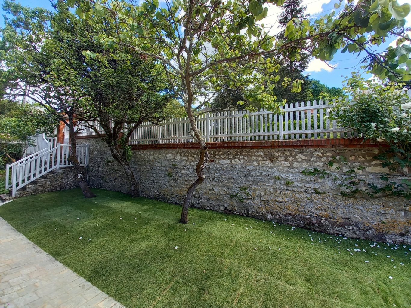Gazon de placage Jardin bien entretenu avec un mur en pierre et une clôture blanche.