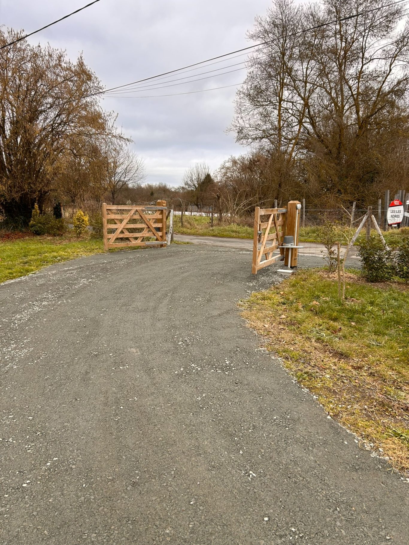 Portail d'écurie - Zone inondable Chemin gravelé menant à une porte en bois ouverte, entouré d'arbres.