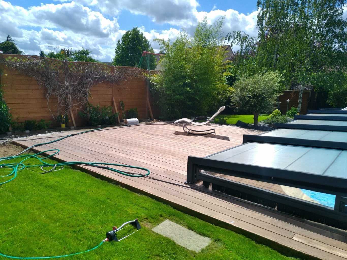 Terrasse en Cumaru Terrasse en bois avec chaise longue, gazon vert et ciel nuageux.
