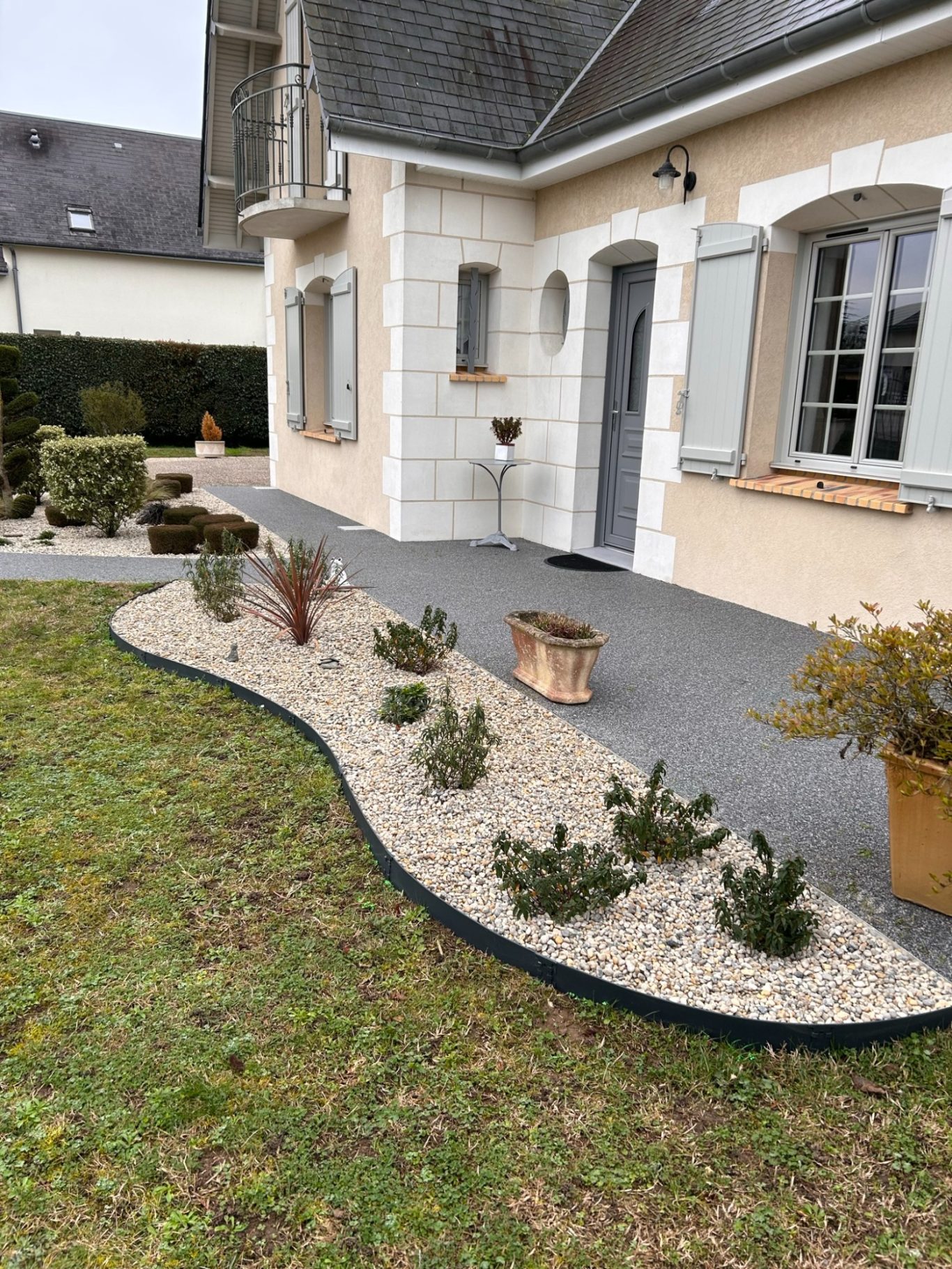 Massif Jardin avec allée en gravier, plantes en pot et mur de maison en arrière-plan.