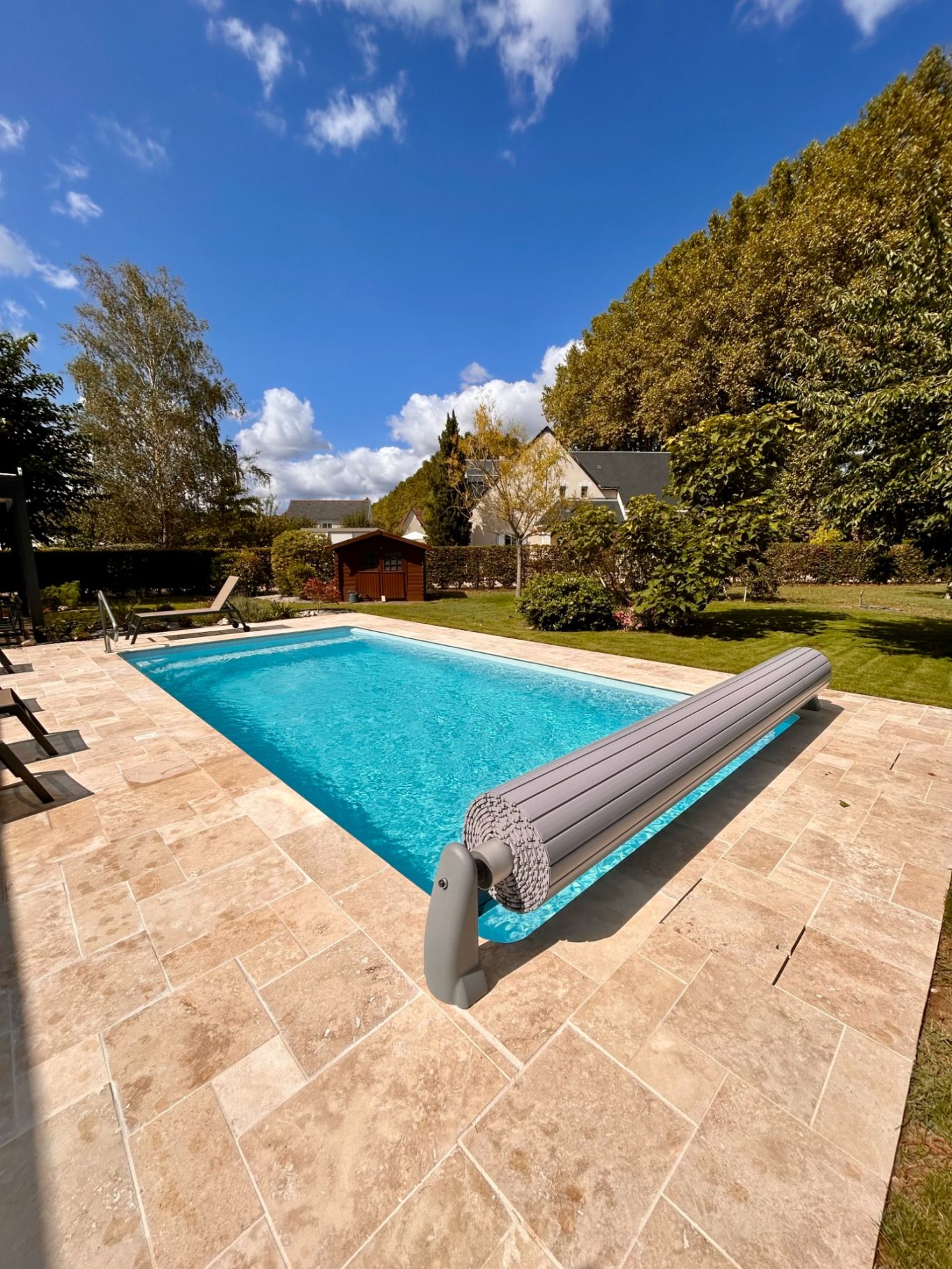 Pose du volet roulant Piscine bleue entourée de verdure, avec des chaises longues au bord.