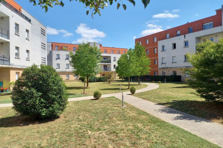 Espace vert avec arbres et bâtiments résidentiels sous un ciel bleu.