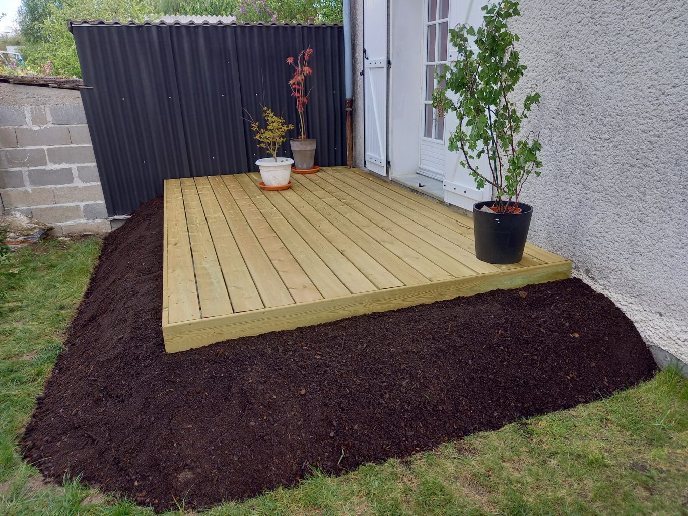 Terrasse en pin classe 4 Terrasse en bois sur sol en terre, entourée de plantes en pots.