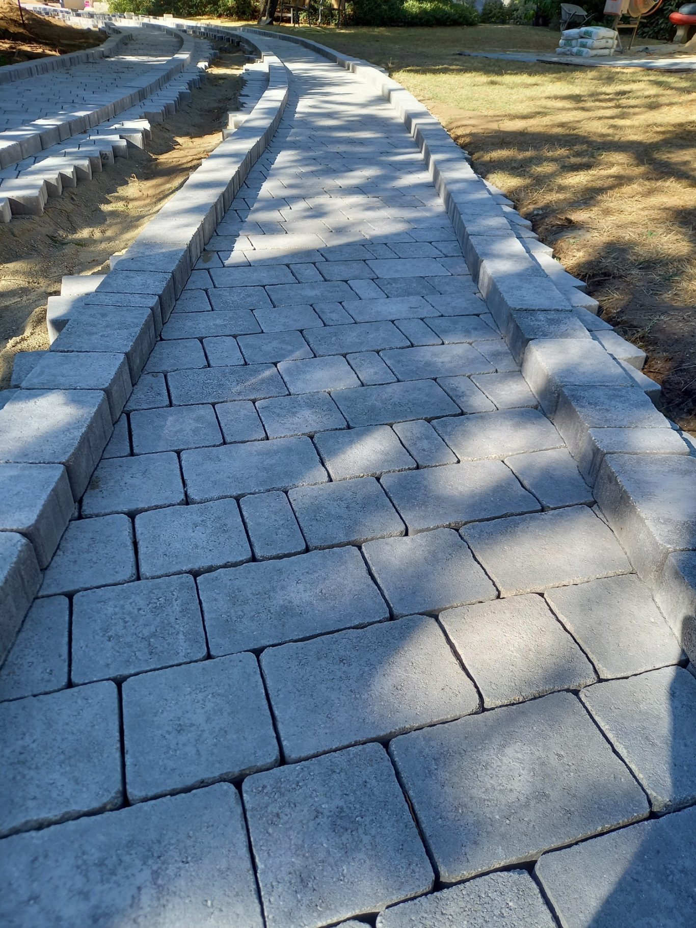 Implantation bordure pour découpe Chemin en pavés gris, bien alignés, entouré de verdure.