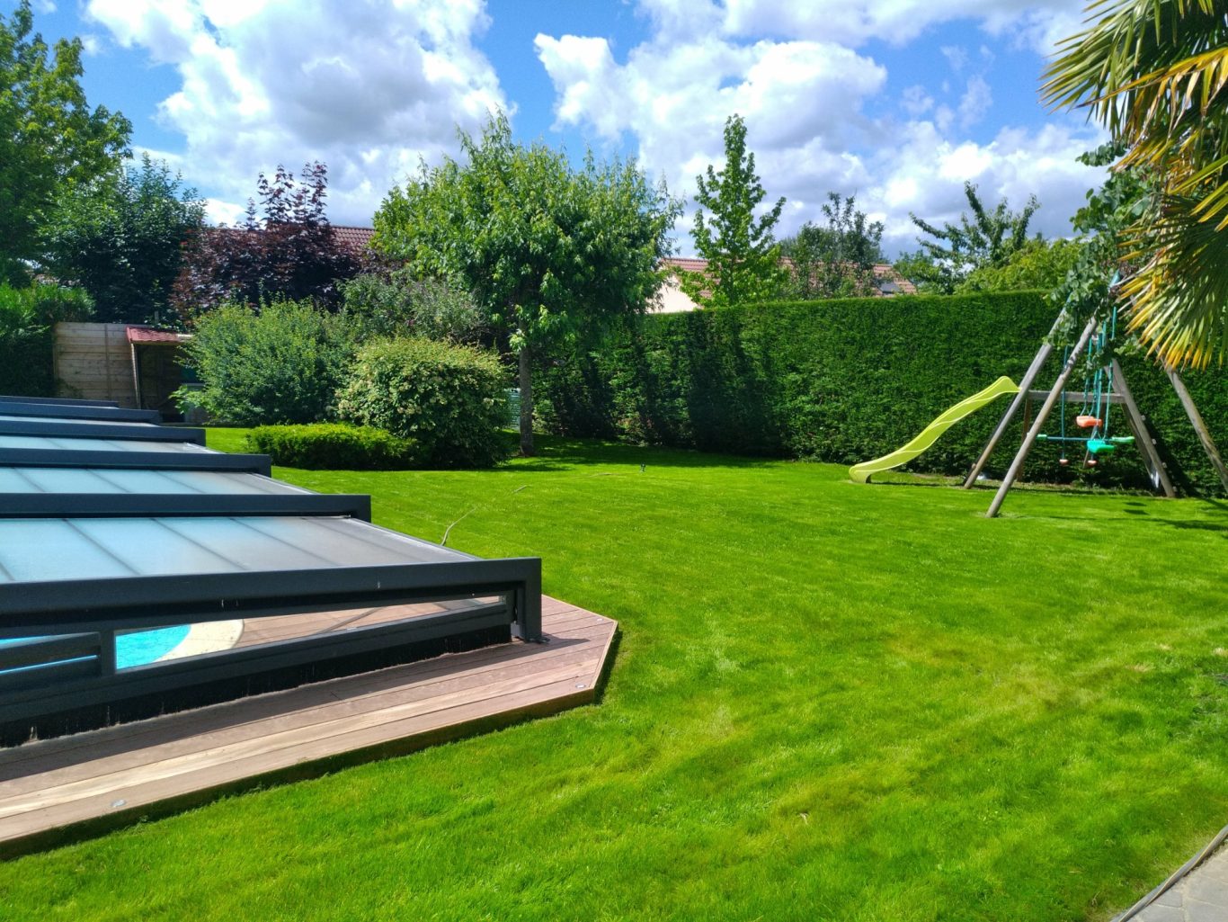 Semi de gazon Jardin verdoyant avec pelouse, piscine, et toboggan. Ciel nuageux en arrière-plan.
