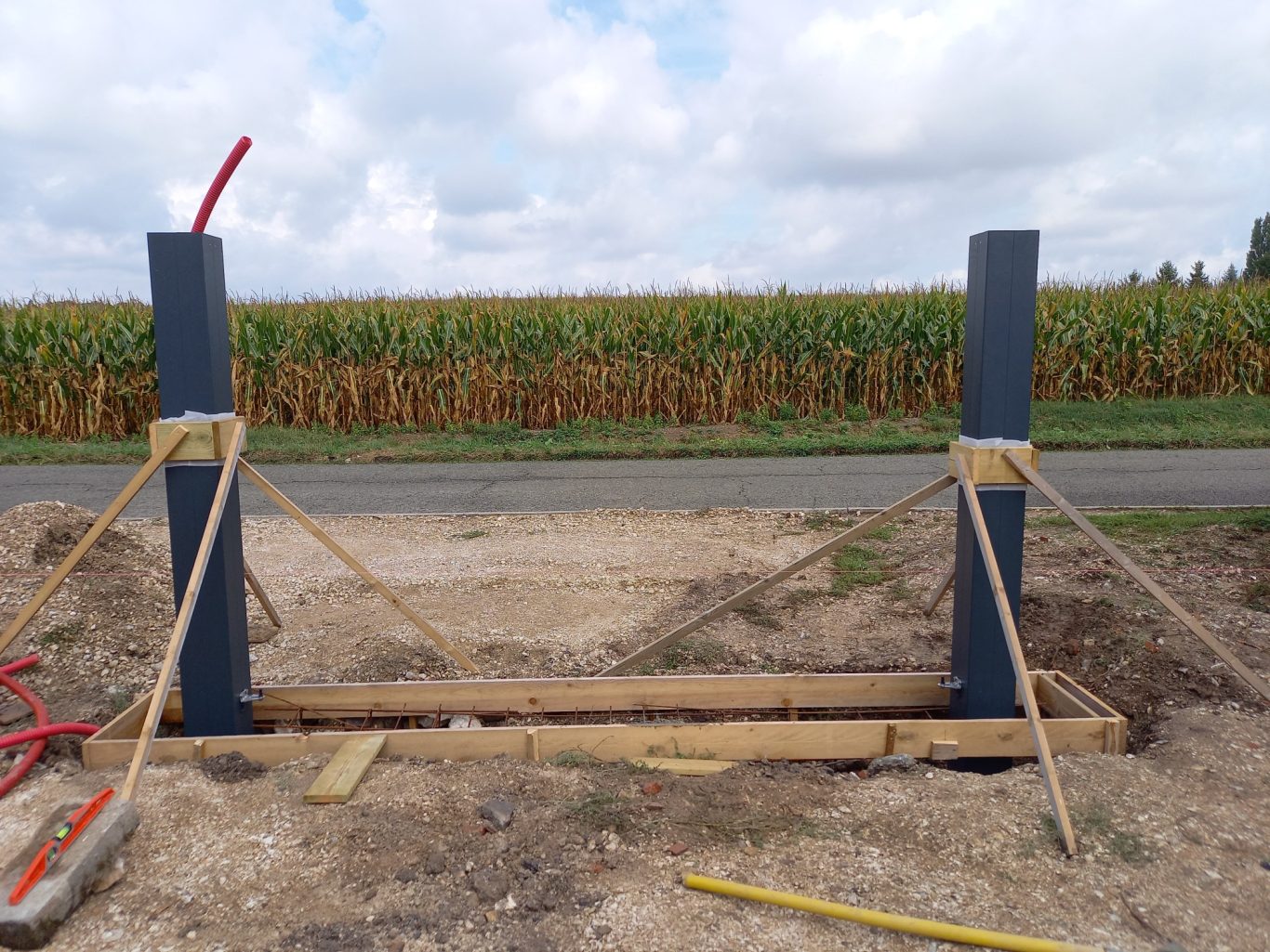 Coffrage du seuil / Mise en place des poteaux Poteau pour une structure, avec des supports en bois, près d'un champ de maïs.