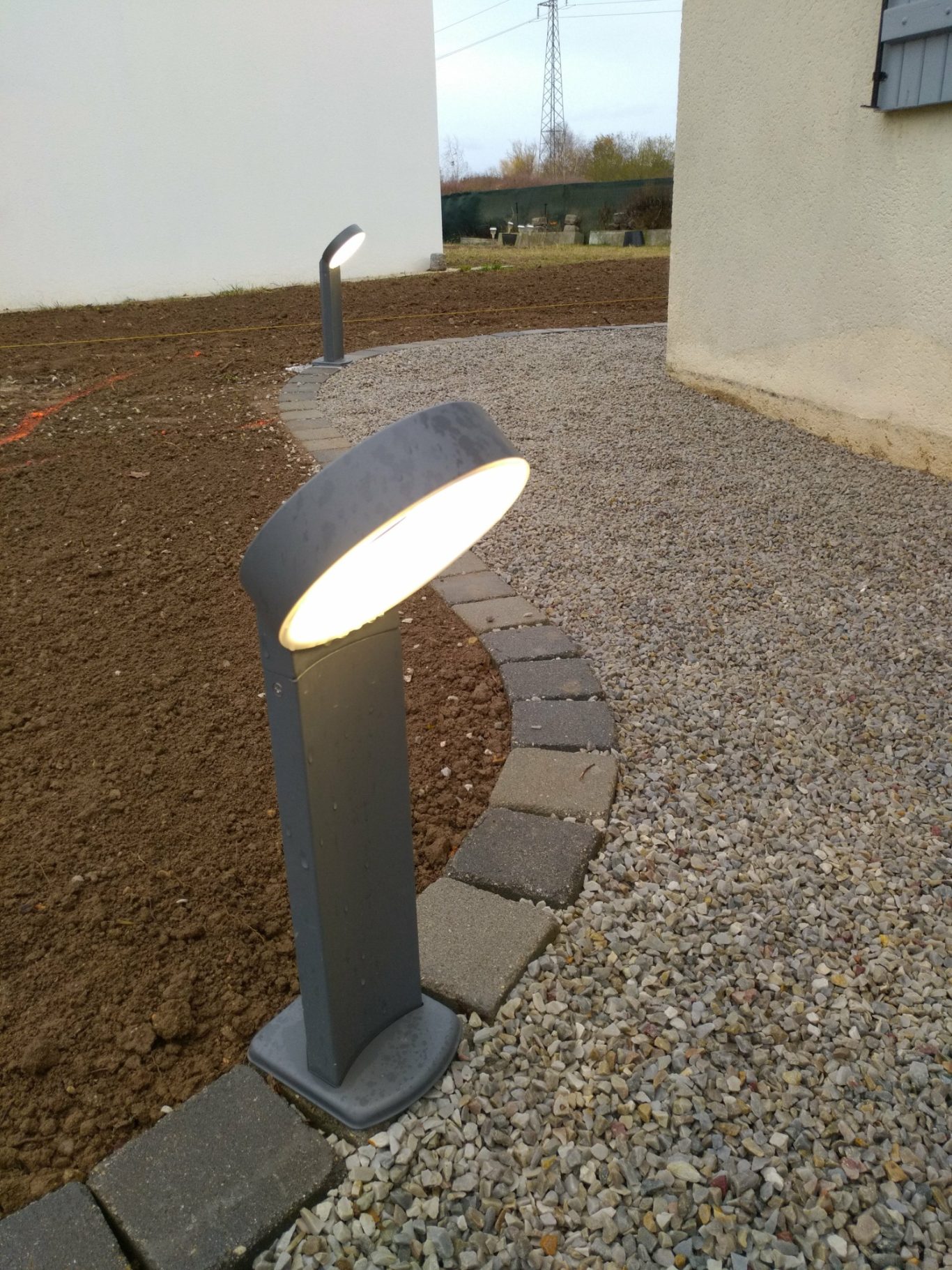 Borne pour allée Borne lumineuse moderne sur un chemin de gravier, entourée de terre.