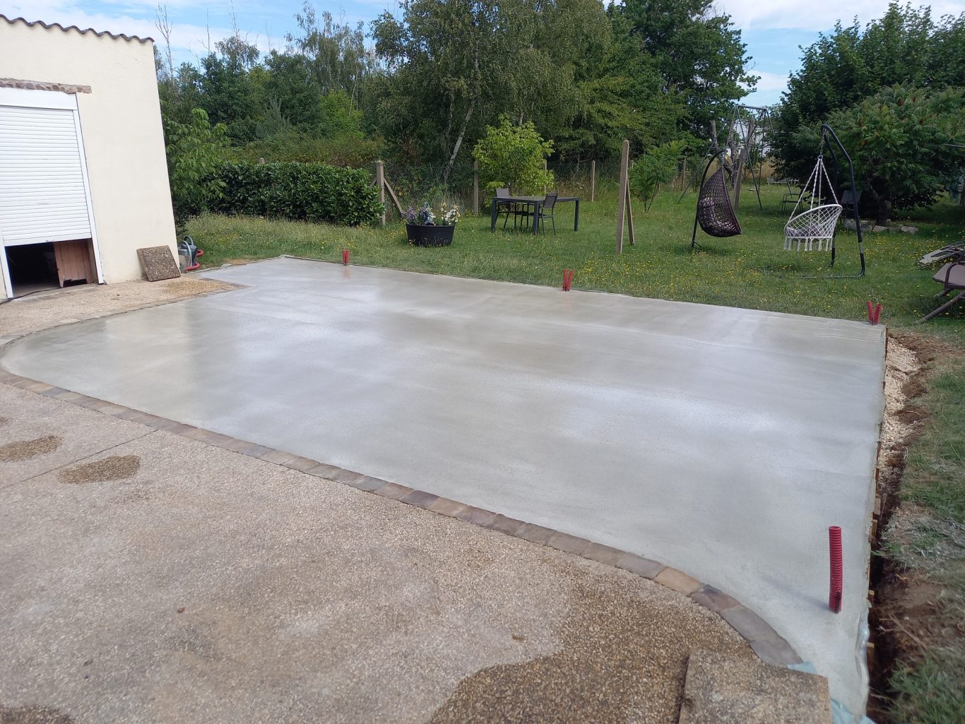 Agrandissement d'une terrasse Surface en béton frais dans une zone de chantier, entourée de verdure.