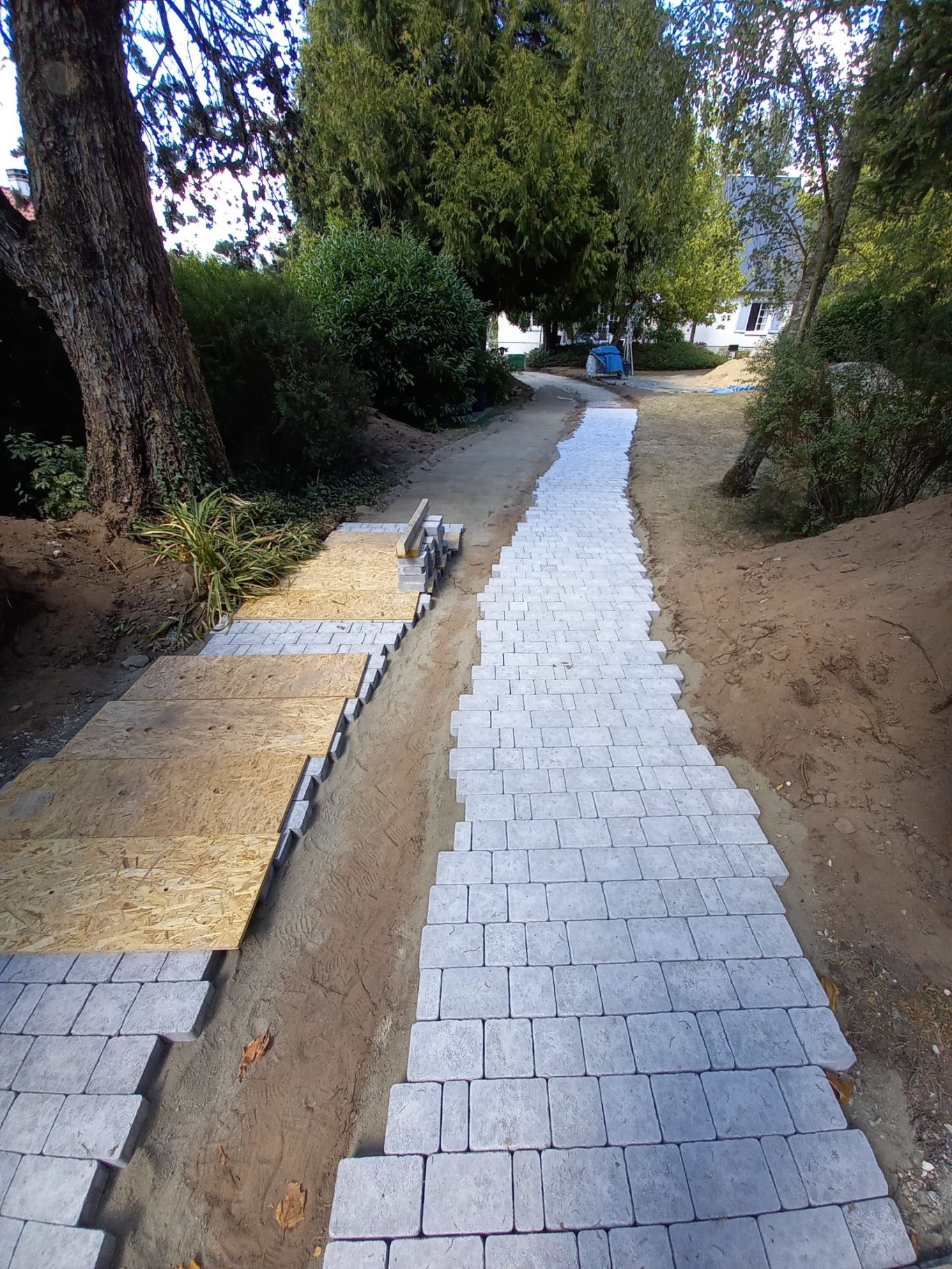 Pose des pavés sur support sable/ciment Chemin sinueux avec des pavés, bordé d'arbres et de verdure.