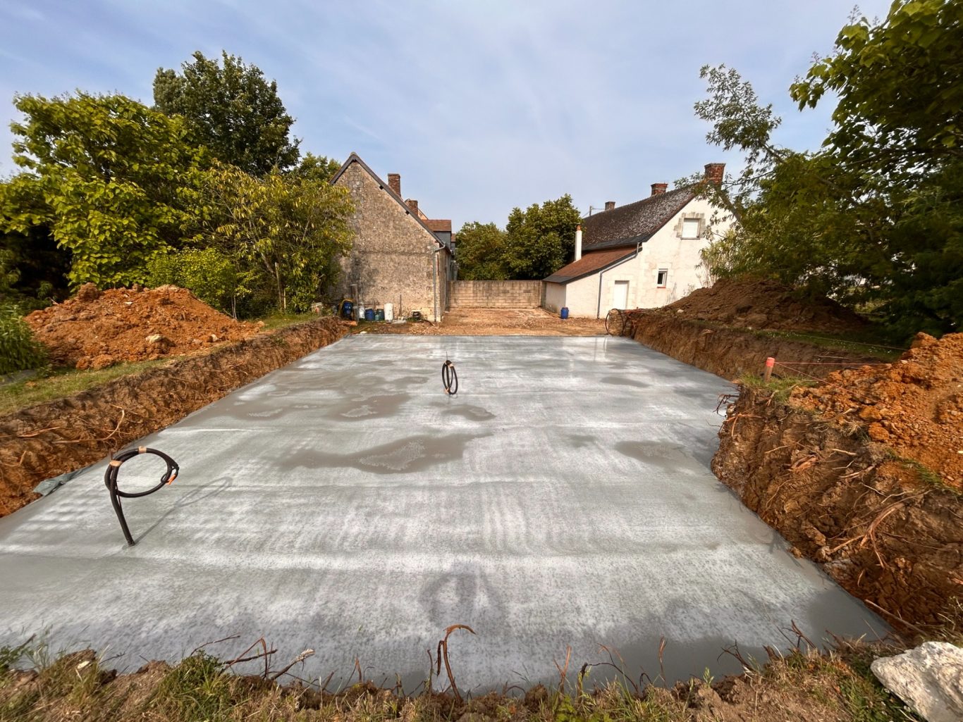 Dalle béton avec arrivée électrique Chantier avec dalle en béton et maisons en arrière-plan. Terrain en préparation.