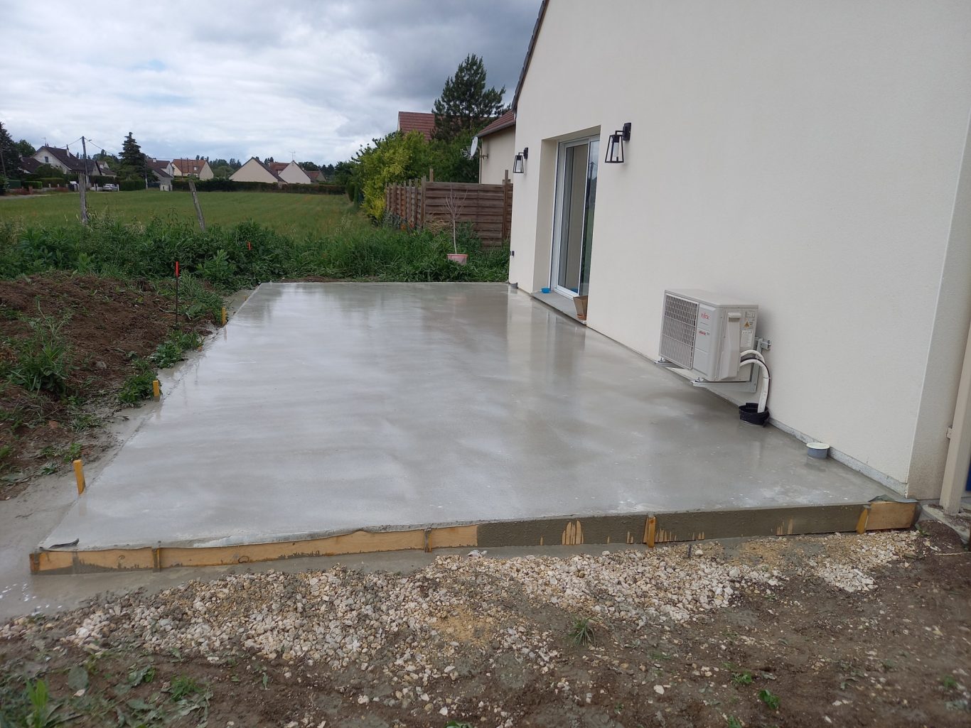 Dalle béton Terrasse en béton fraîchement coulée, avec un jardin en arrière-plan.