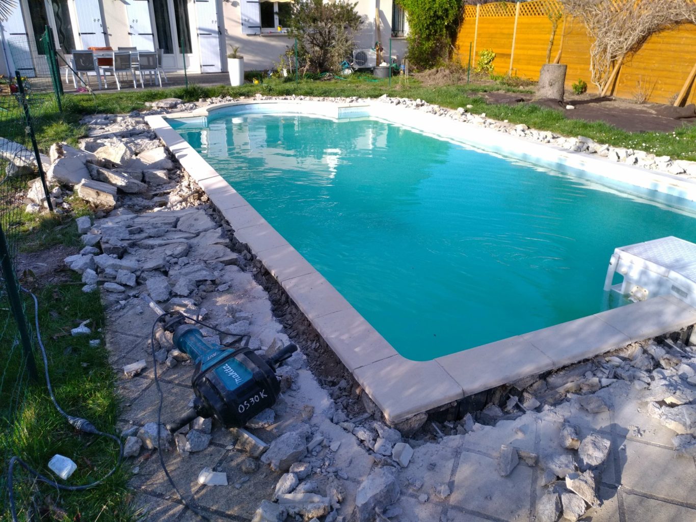 Démolition Piscine en travaux avec des pierres autour et de l'eau turquoise.