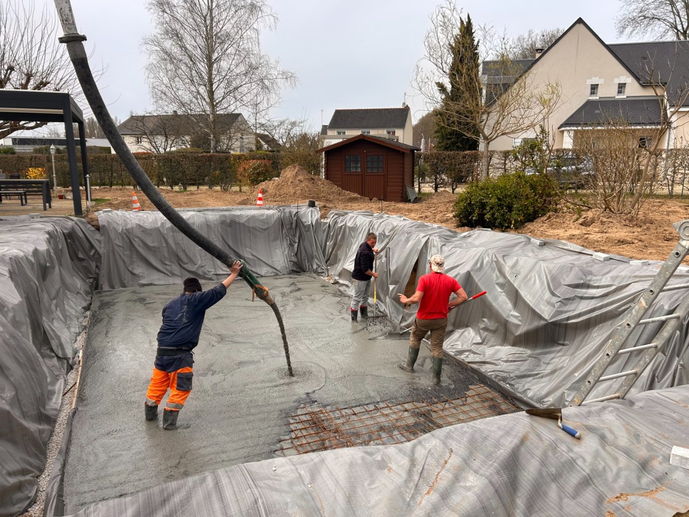 Coulage dalle de fond Trois ouvriers versent du béton dans une piscine en construction.
