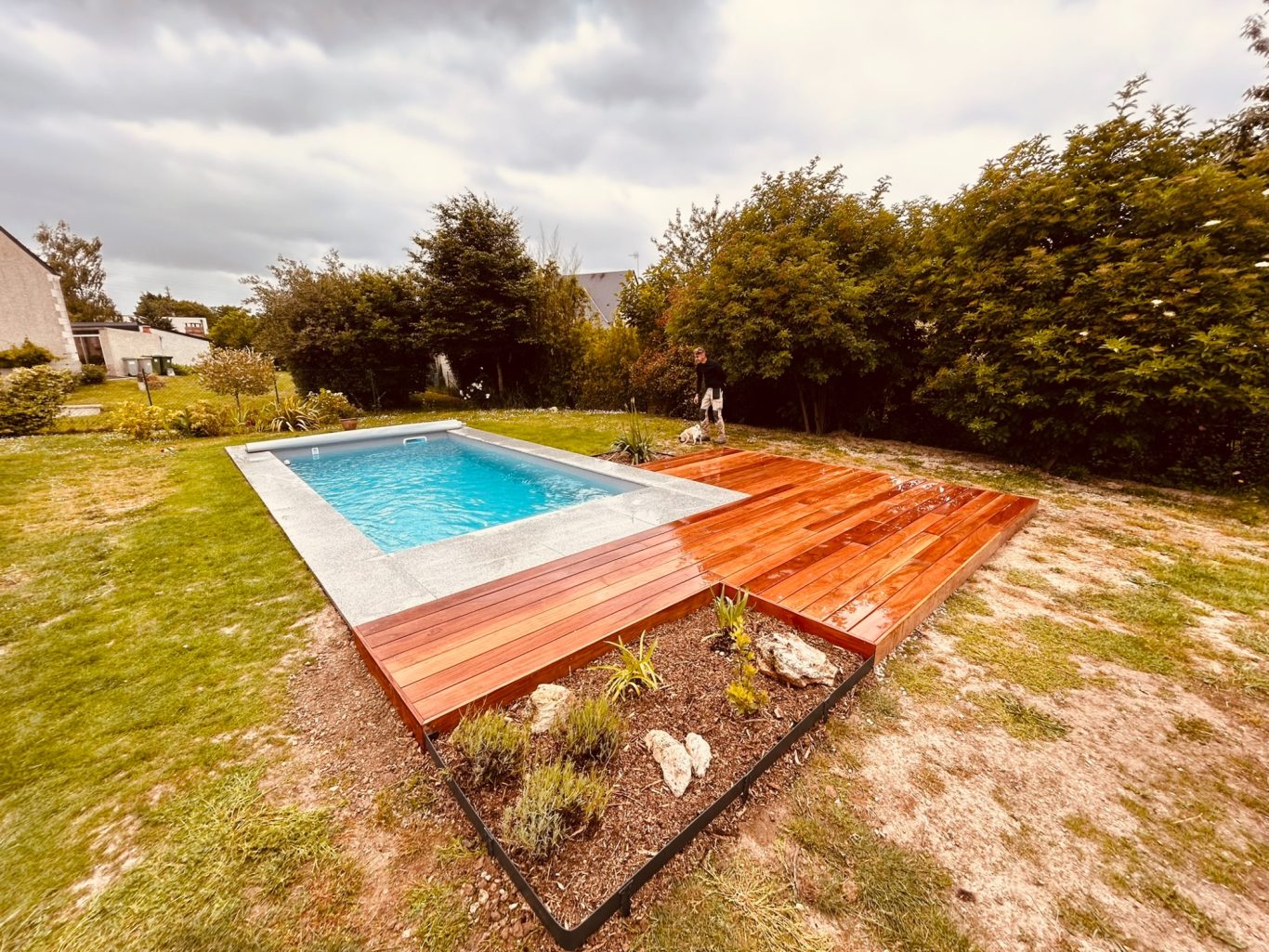 Terrasse en Cumaru Piscine avec terrasse en bois entourée de verdure et d'arbres. Ciel nuageux.
