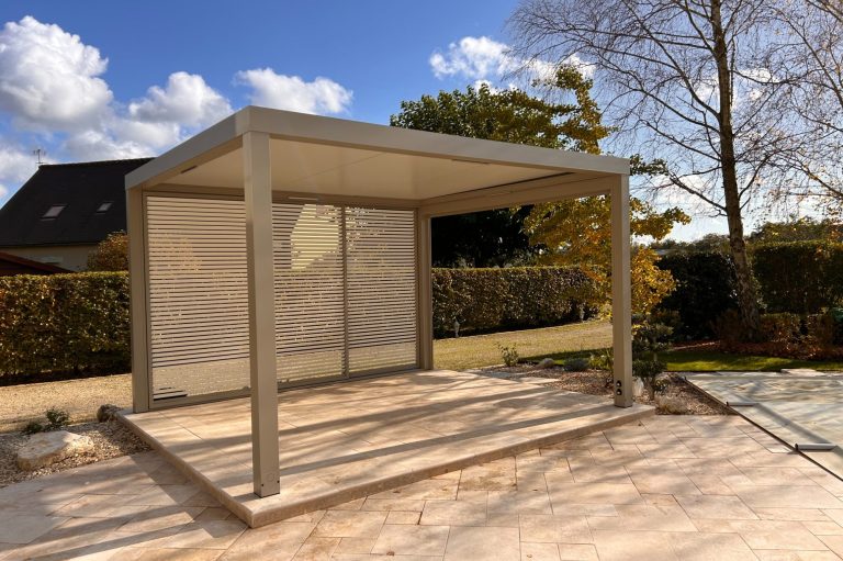 Abri moderne en béton, avec des murs en lames et un ciel bleu parsemé de nuages.
