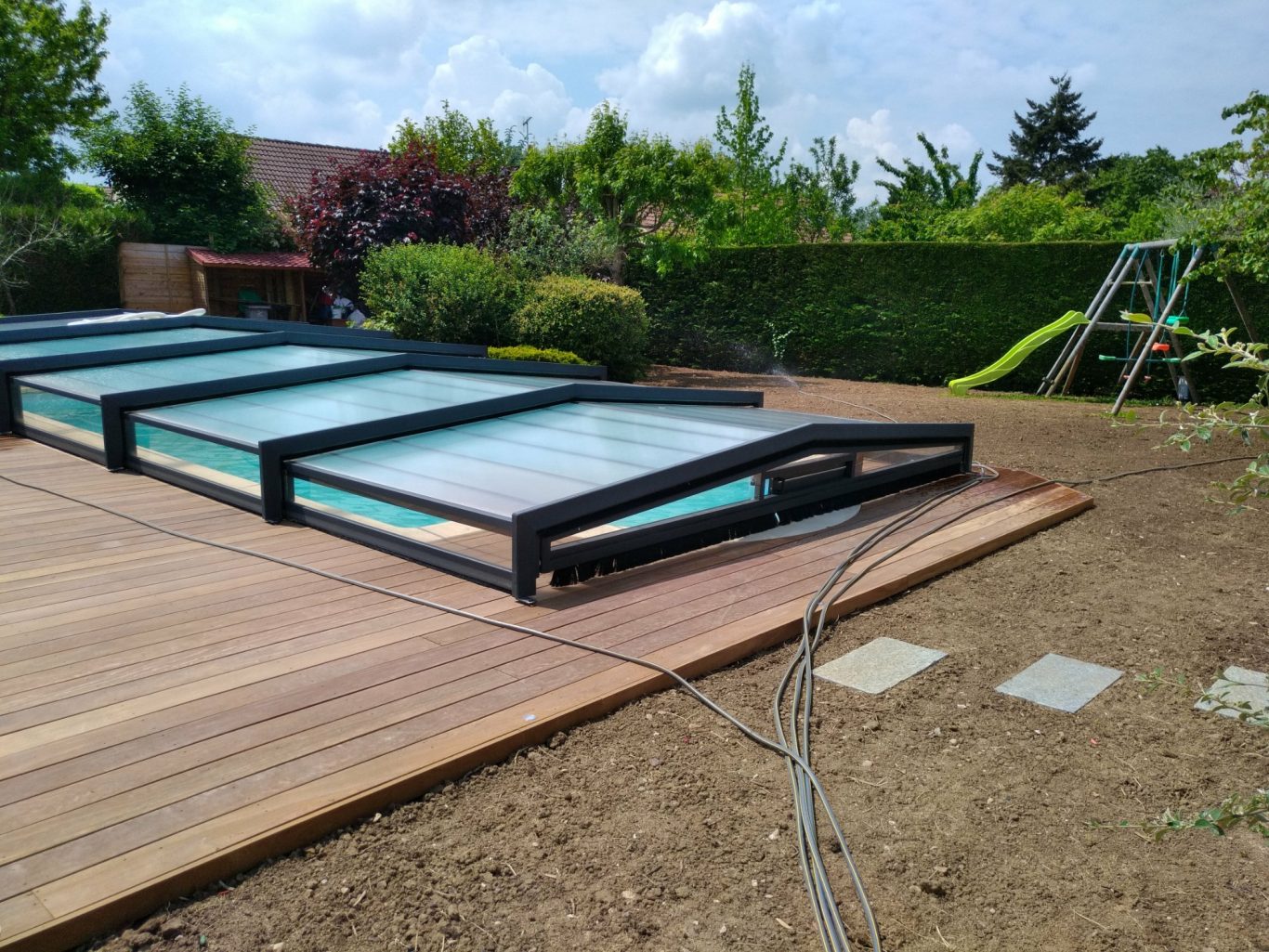Structure finale Couverture de piscine partiellement fermée sur un deck en bois dans un jardin.
