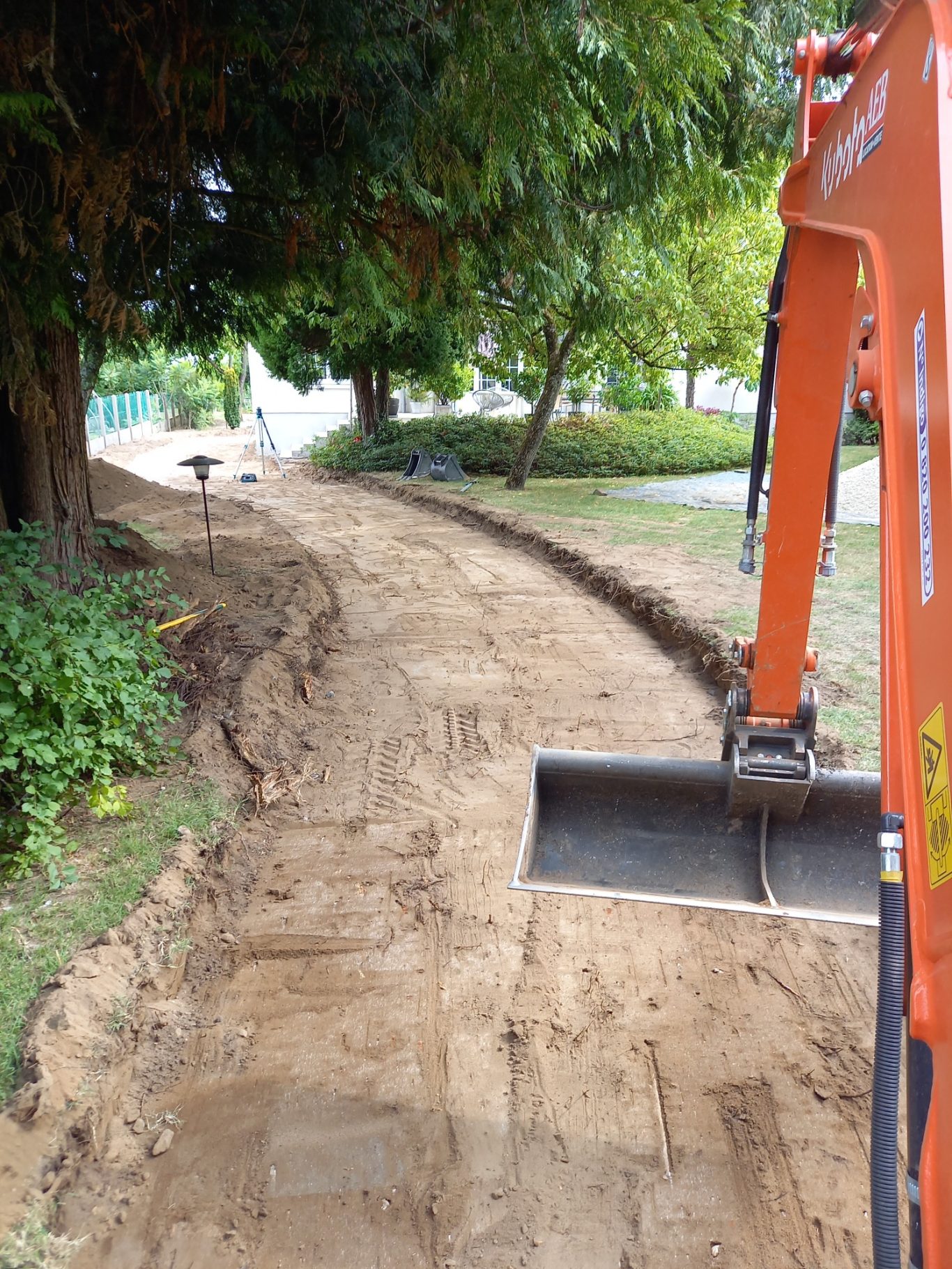 Démolition / Nivellement Tranchée en cours de creusement, bordée d’arbres et d’herbe, avec une pelle mécanique.