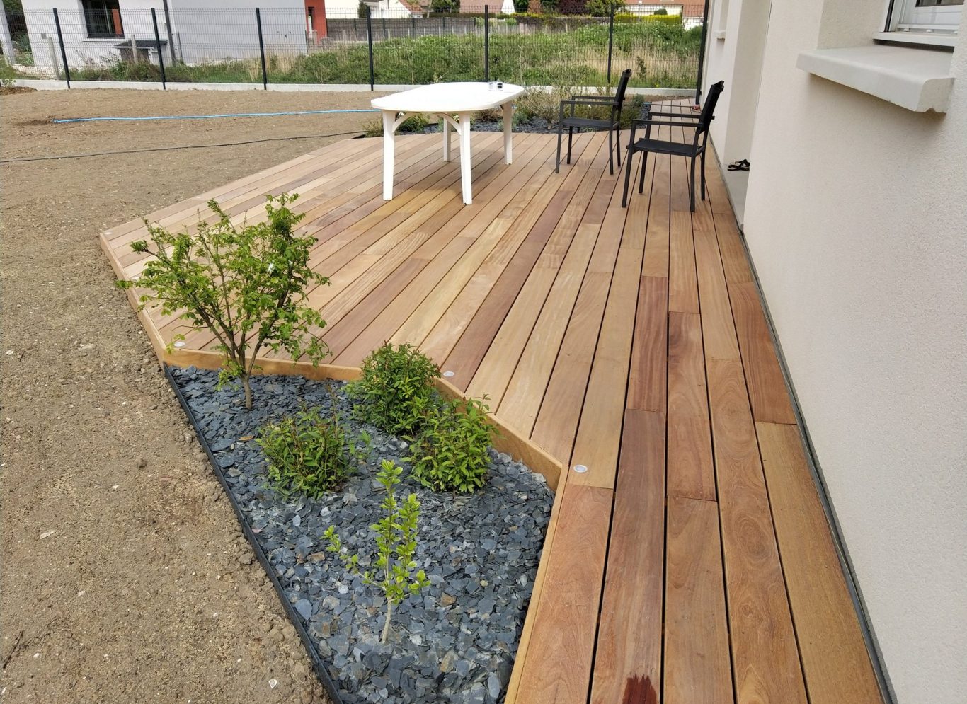 Terrasse en bois avec des plantes et des pierres décoratives, table et chaises noires.