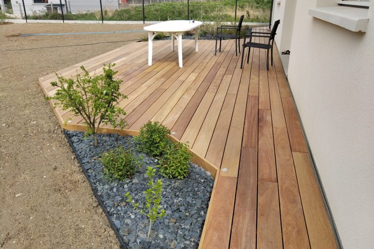 Terrasse en bois avec des plantes et une table, située à proximité d'une maison.