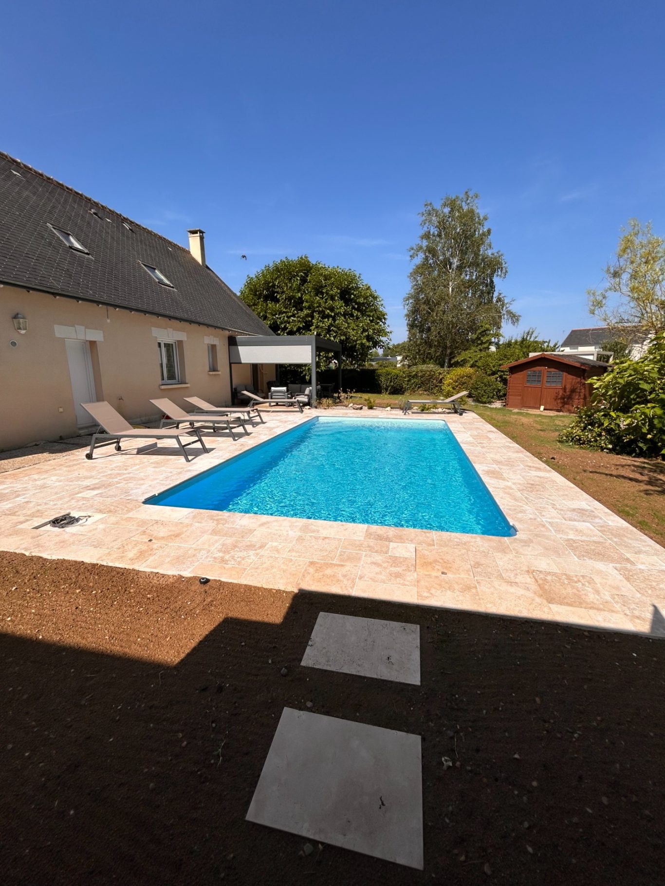 Piscine en service Piscine bleue entourée de chaises longues et de verdure, ciel dégagé.