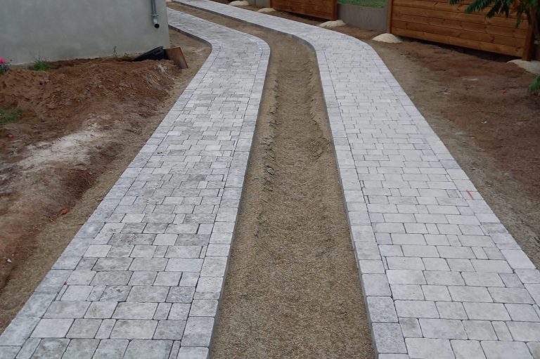 Chemin en pavés blancs avec sections en terre, entouré de terre et de gravier.