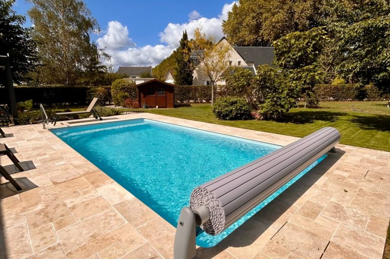 Piscine éclairée entourée d'un patio en pierre, arbres en arrière-plan.