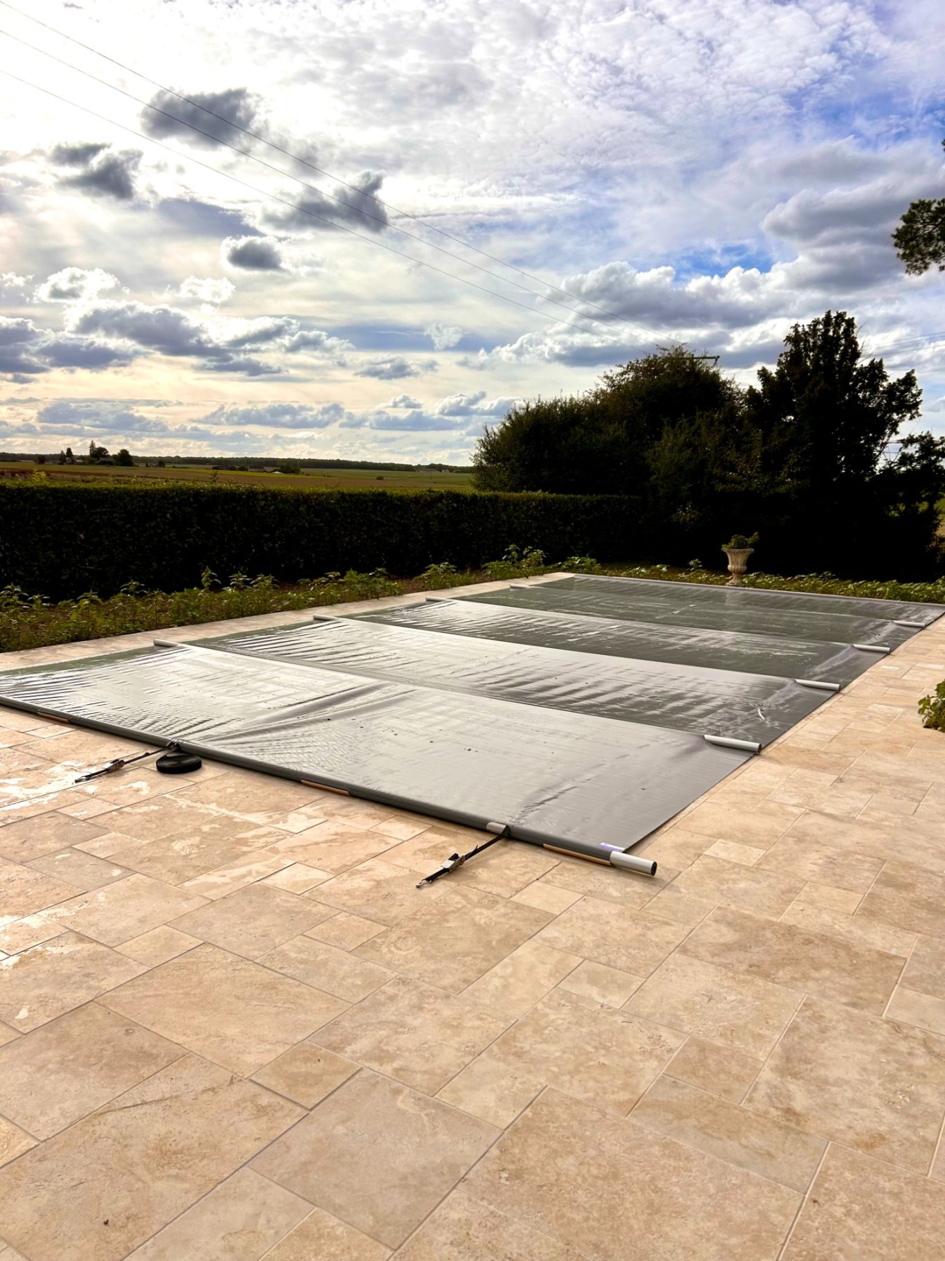 Bâche à barre Couverture de piscine grise sur un patio, ciel nuageux en arrière-plan.